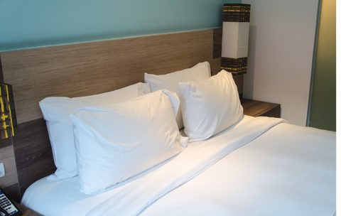 A bed in a hotel room featuring the Extra Plump DuPont Polyester Pillow by The Pillow Factory for added support.
