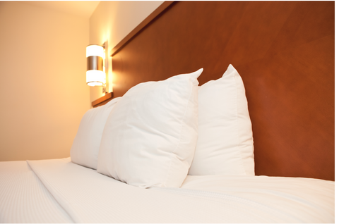 A bed with white pillows made of Extra Plump DuPont Polyester Pillows by The Pillow Factory and a lamp.