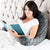 A woman reading a book in bed with a Malouf Lounge Pillow for added comfort.