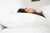 A woman sleeping in a bed with white sheets and a Down Etc. 50% White Goose Down / 50% White Goose Feather Pillow from Down Etc. for a Supportive Sleep Experience.