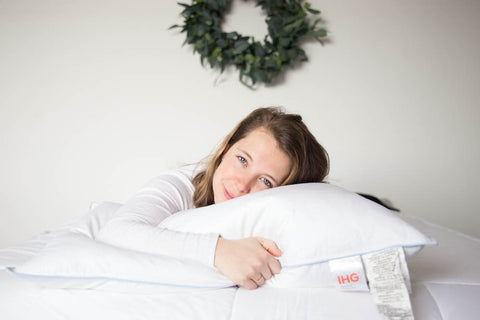 A woman laying on a Holiday Inn® Touch of Down Feather & Down Pillow | Soft Support by Hollander.