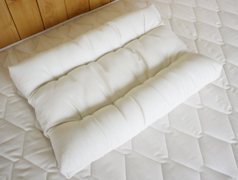 A white Holy Lamb Organics Orthopedic Neck Pillow - Standard Size on the bed provides neck support.