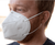 A man with short red hair and a beard is wearing a white pillowsdotcom Final Sale: KN95 Face Mask | 20 Pack. The mask covers his nose and mouth and is secured with ear loops. He is looking to the right side of the image. The background is blurred and light-colored. Final Sale: No returns or exchanges.