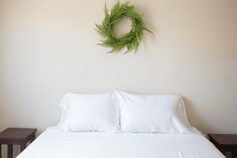 A white bed with a fern wreath on the wall, accented by a Pillowtex Copper Infused Bamboo Pillowcase for added comfort.