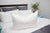 A Pillowtex High End White Goose Down pillow rests on a bed in a bedroom.