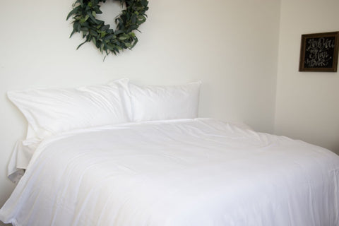 A white bed with a wreath hanging on the wall and a Pillowtex Bamboo Duvet Cover for Weighted Blanket.