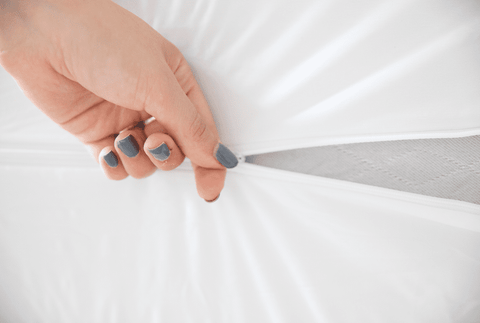 A woman's hand is opening a zipper on a Pillowtex Deluxe Mattress Protector from Pillowtex.