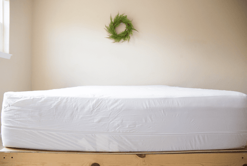 A white mattress on top of a wooden bed frame, protected by a Pillowtex Deluxe Mattress Protector.