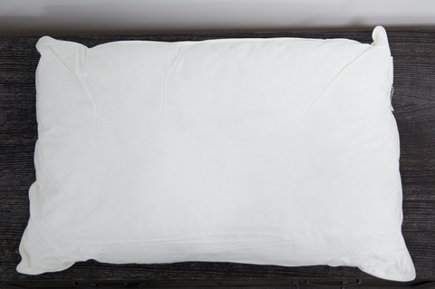 A firm white Pillowtex Down Alternative Pillow | Medium sits on the wooden table.