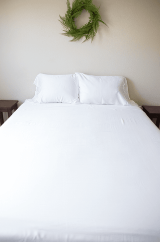 A white bed with a Pillowtex Copper Infused Bamboo pillowcase hanging above it.