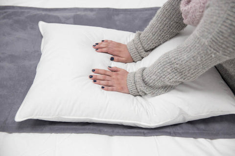 A woman's hands resting on a Pillowtex Like Down Pillow by Pillowtex on a bed.
