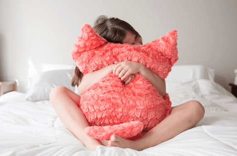 A girl cuddling a pink Pillowtex Plush Cat Ear Throw Decorative Pillow Cover on a bed.