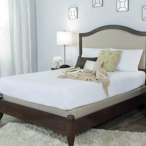 A bed in a bedroom with a wooden headboard, featuring a Protect-A-Bed Mattress Protector for added protection.