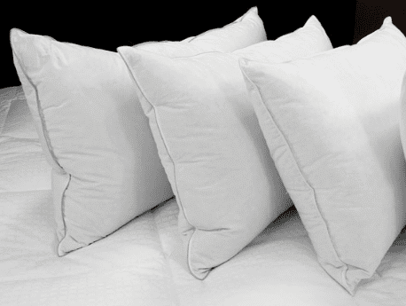 Four Temperloft Down/Down Alternative Pillows from Sysco Guest Supply sitting on top of a bed.