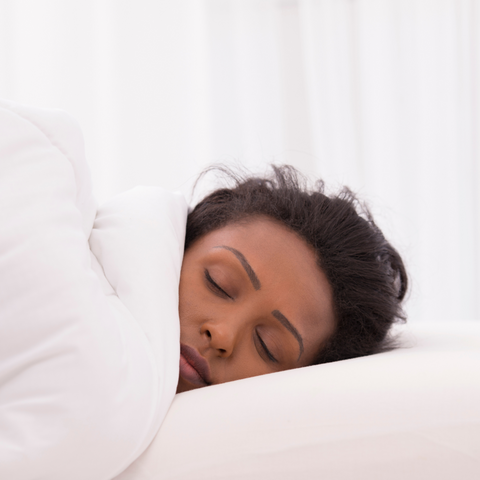 A woman sleeping on a bed with a Pillowtex Triple Core White Duck Down & Feather Pillow.